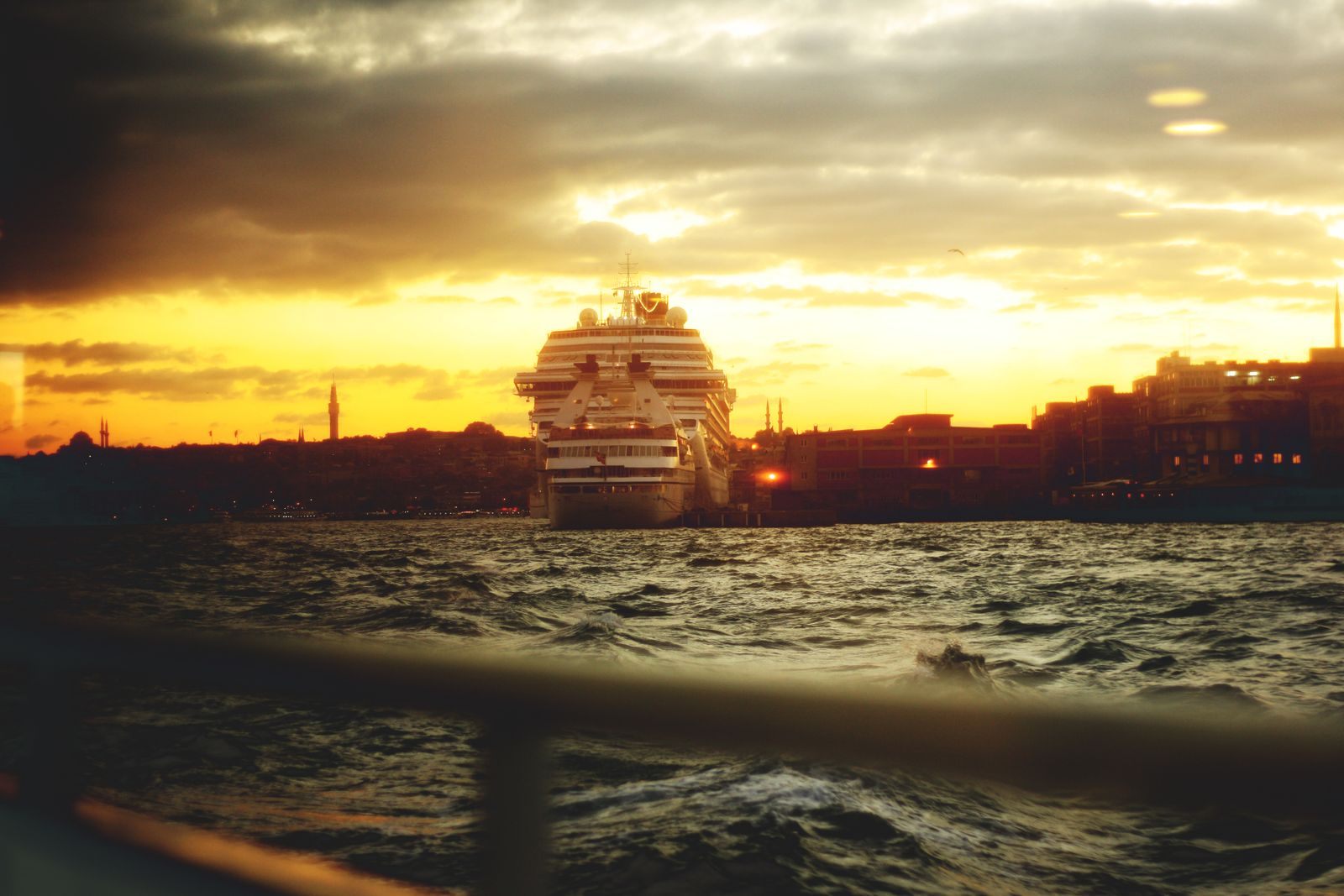 Cruise ship silhouetted off a city coastline at sunset