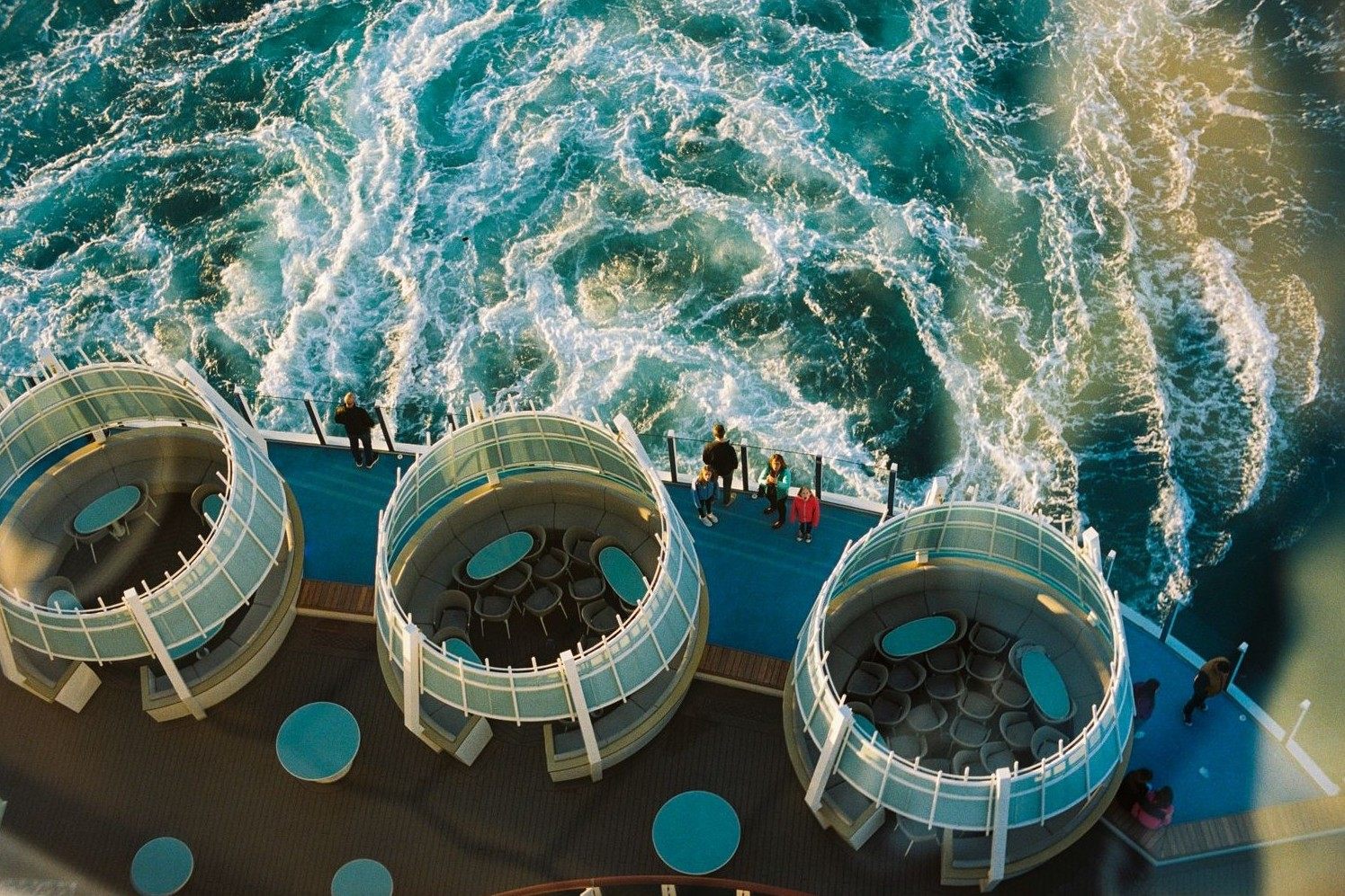 Looking down from a cruise ship onto stern-deck seating pods above the wake, where cruise line policy changes play out